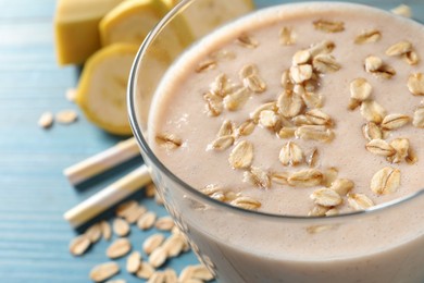 Photo of Glass of tasty banana smoothie with oatmeal on light blue table, closeup