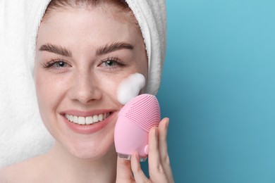 Photo of Young woman washing face with brush and cleansing foam on light blue background, closeup. Space for text