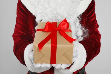 Photo of Santa Claus holding Christmas gift on light grey background, closeup