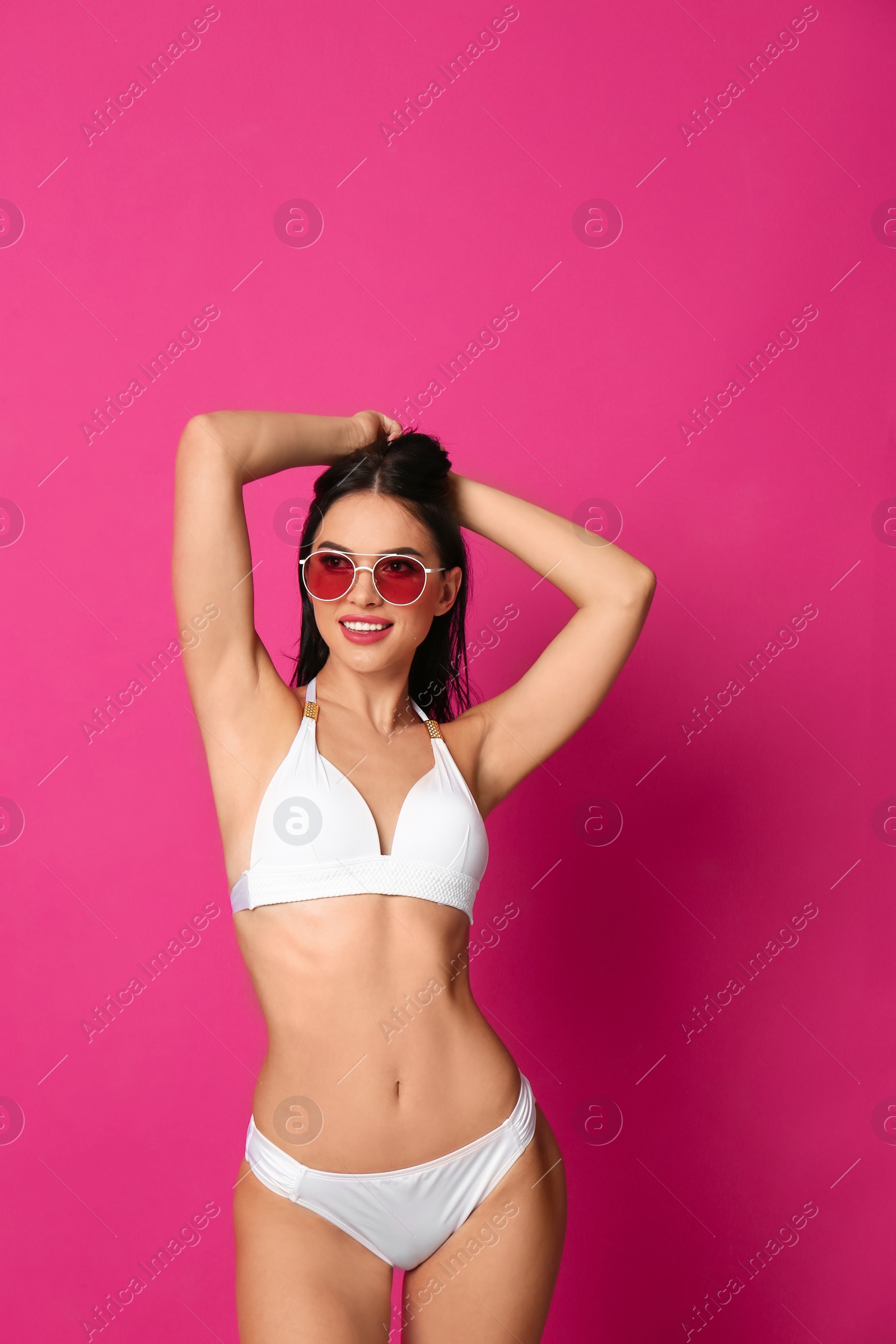 Photo of Beautiful young woman in white bikini with sunglasses on pink background