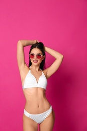 Photo of Beautiful young woman in white bikini with sunglasses on pink background