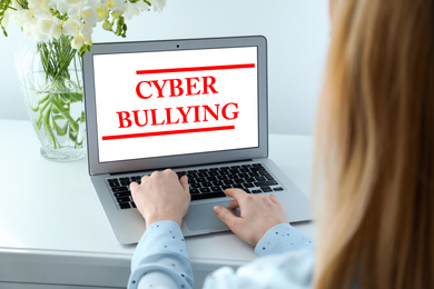 Young woman using laptop at white table, closeup. Cyber bullying