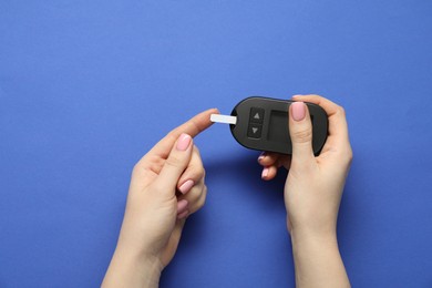 Photo of Diabetes. Woman checking blood sugar level with glucometer on blue background, top view