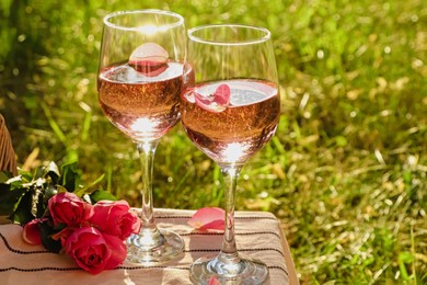 Glasses of delicious rose wine with petals and flowers on white picnic blanket outside