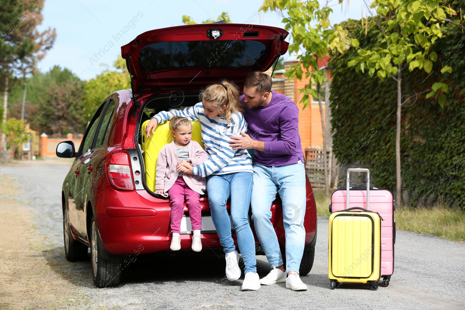 Photo of Young family with suitcases having rest near car trunk outdoors