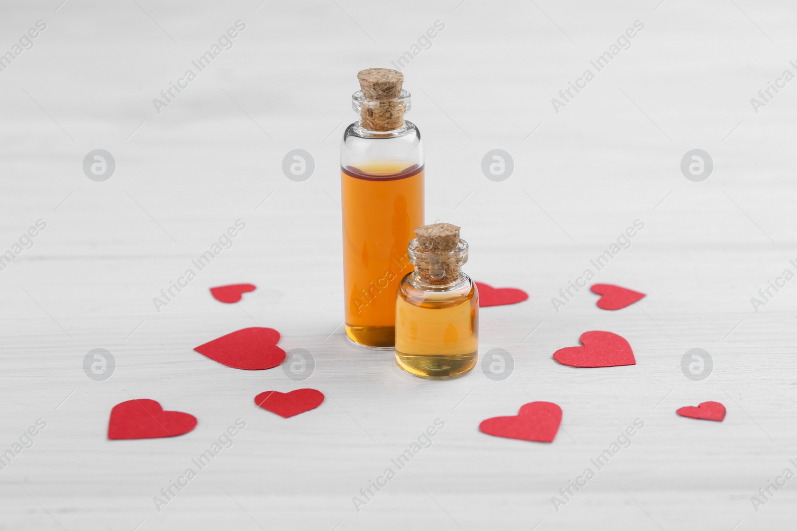 Photo of Bottles of love potion and paper hearts on white wooden table