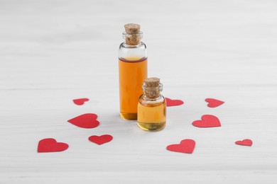 Bottles of love potion and paper hearts on white wooden table