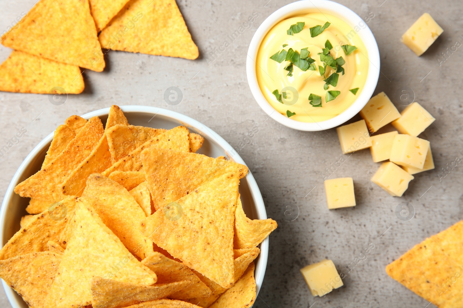 Photo of Bowl of delicious mexican nachos chips and cheese sauce on grey table, flat lay