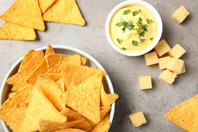 Bowl of delicious mexican nachos chips and cheese sauce on grey table, flat lay