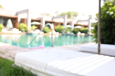 Photo of Sun loungers near outdoor swimming pool, blurred view. Luxury resort