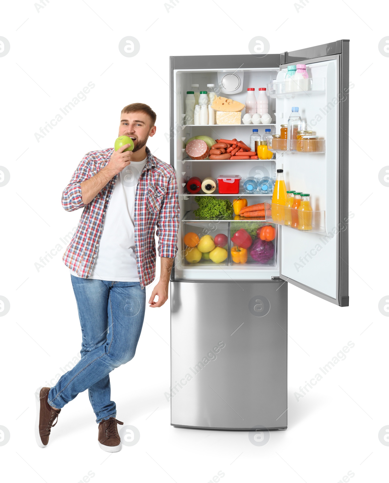 Photo of Young man eating apple near open refrigerator on white background