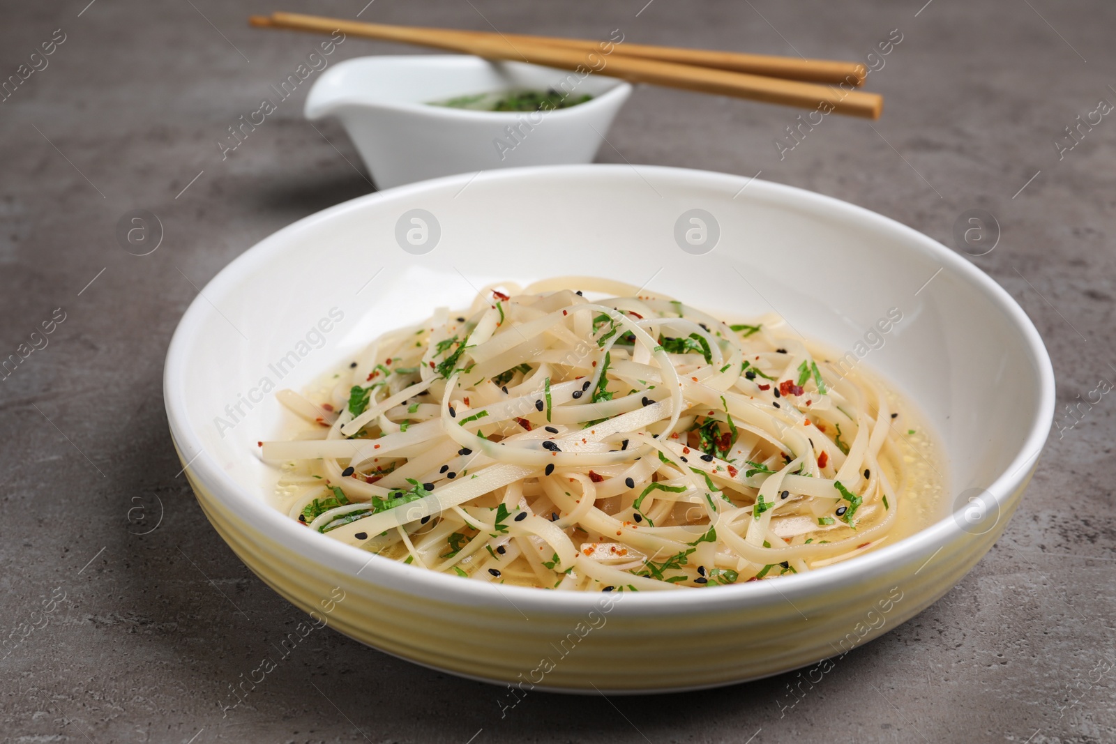 Photo of Plate of noodles with broth and herb on grey background, closeup