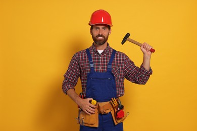 Photo of Professional builder in uniform with hammer and tool belt on yellow background