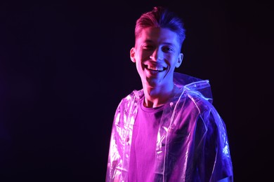 Photo of Young man wearing clear coat on dark background in neon lights. Space for text