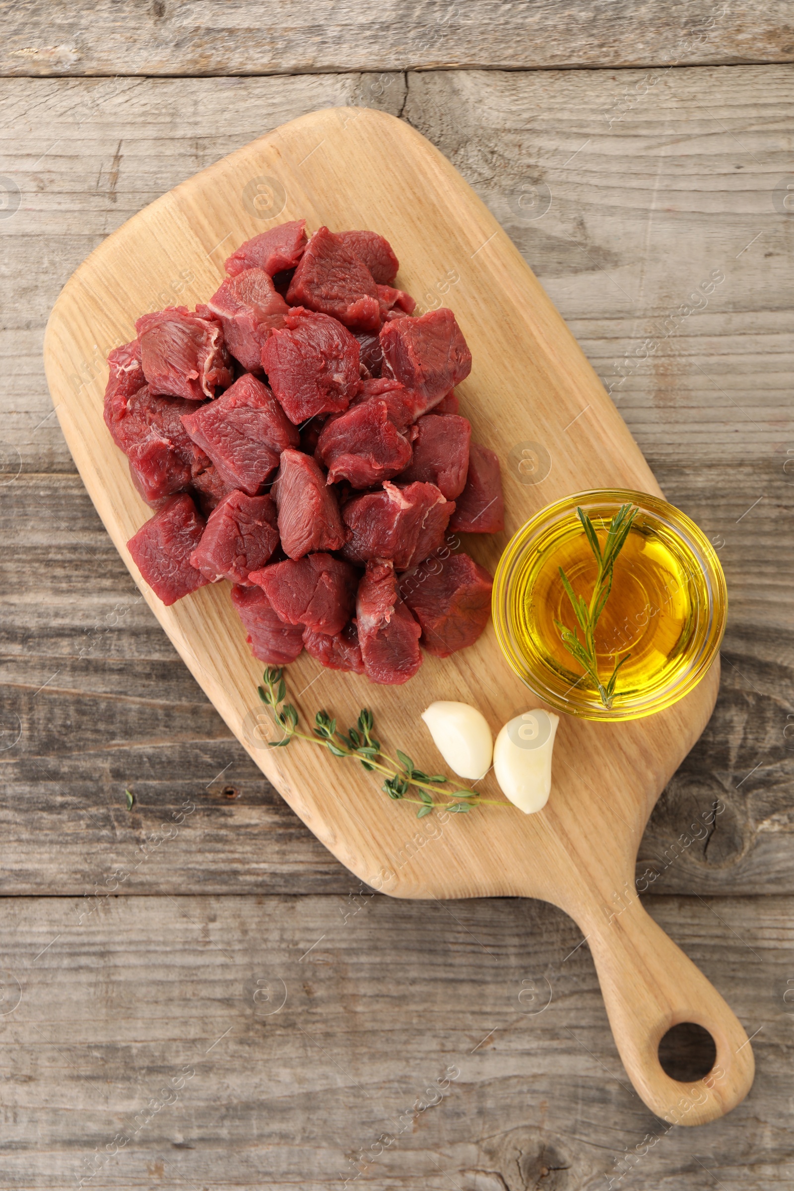 Photo of Pieces of raw beef meat, oil and garlic on wooden table, top view