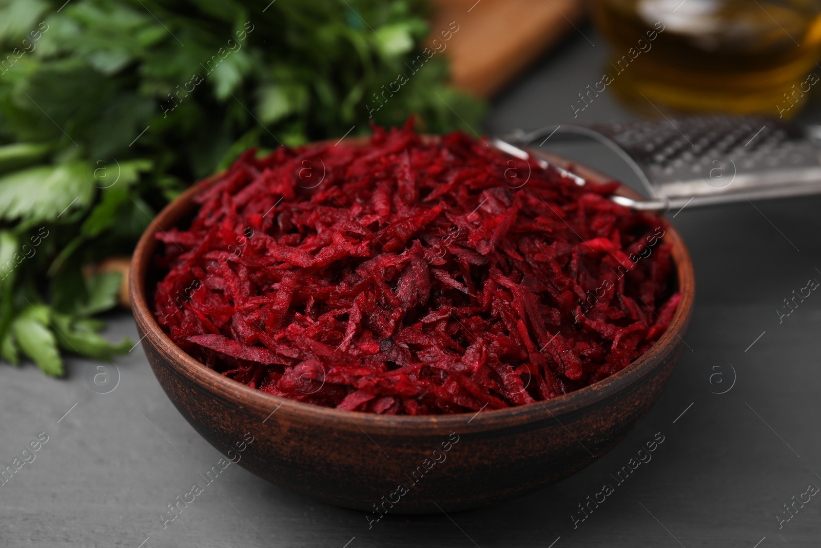 Photo of Grated red beet in bowl on gray table, closeup