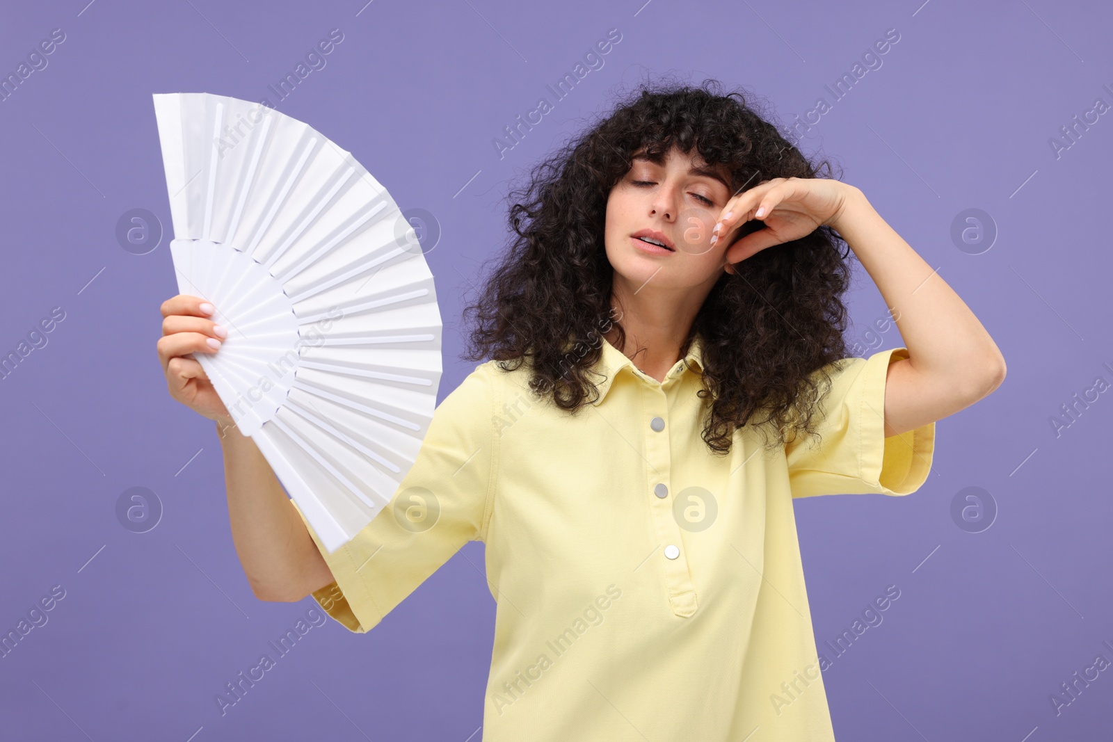 Photo of Woman with hand fan suffering from heat on purple background