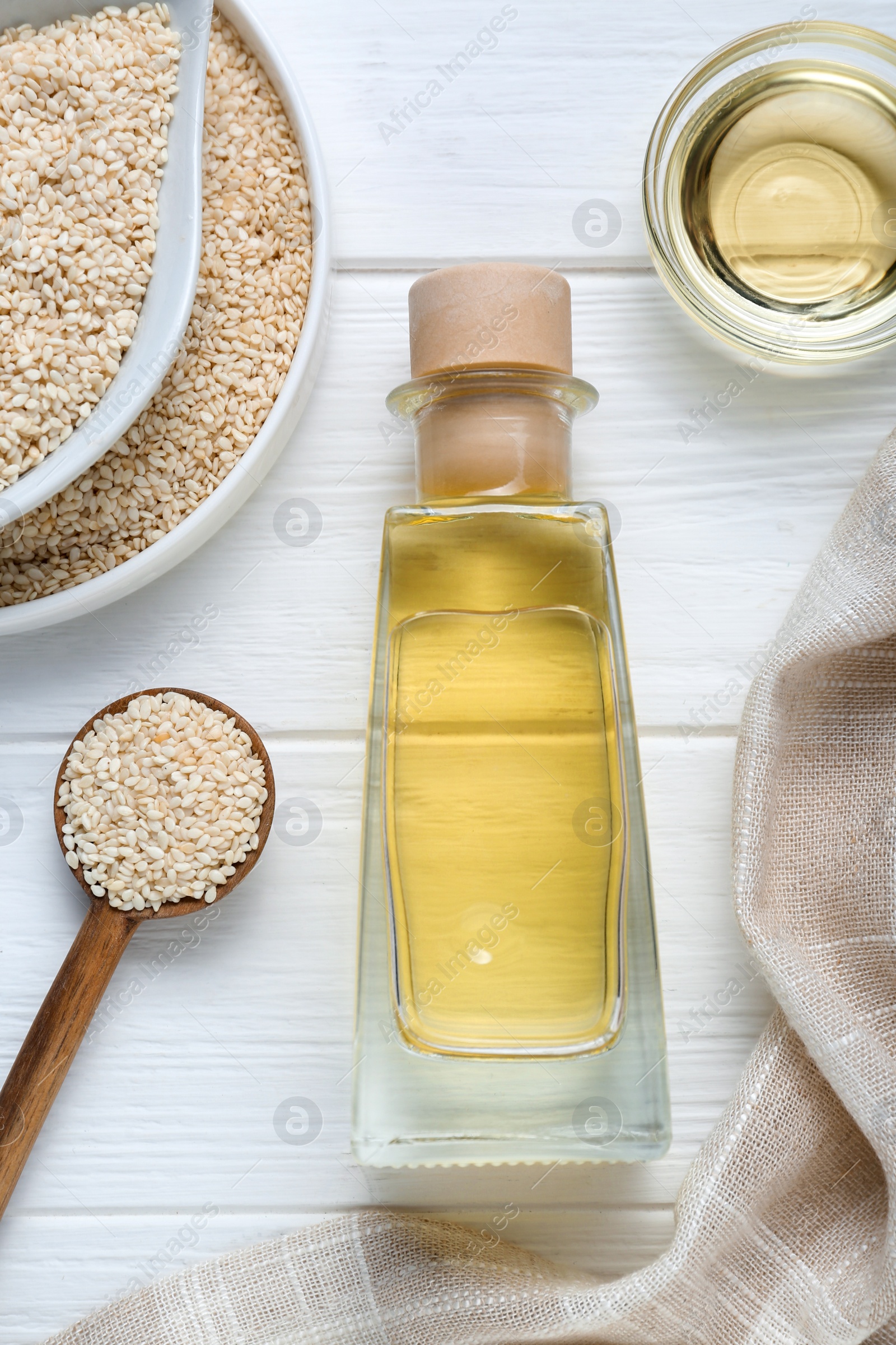 Photo of Sesame oil and seeds on white wooden table, flat lay