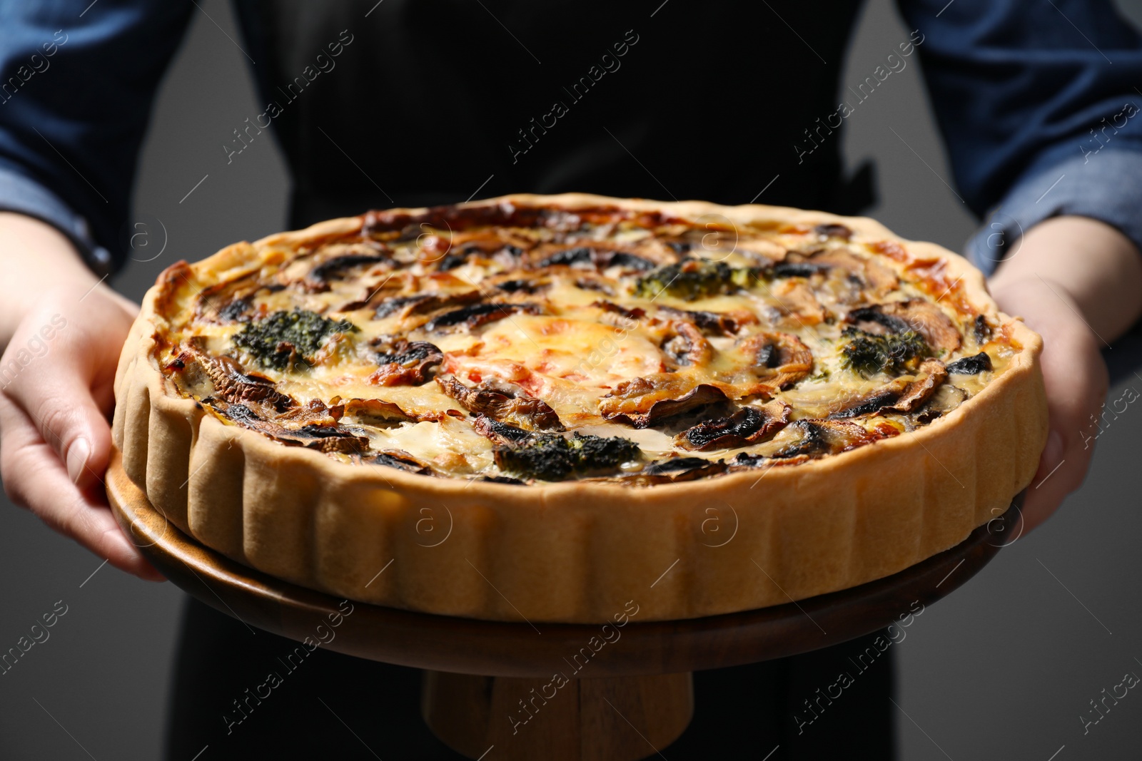 Photo of Woman holding delicious quiche with mushrooms on dark grey background, closeup