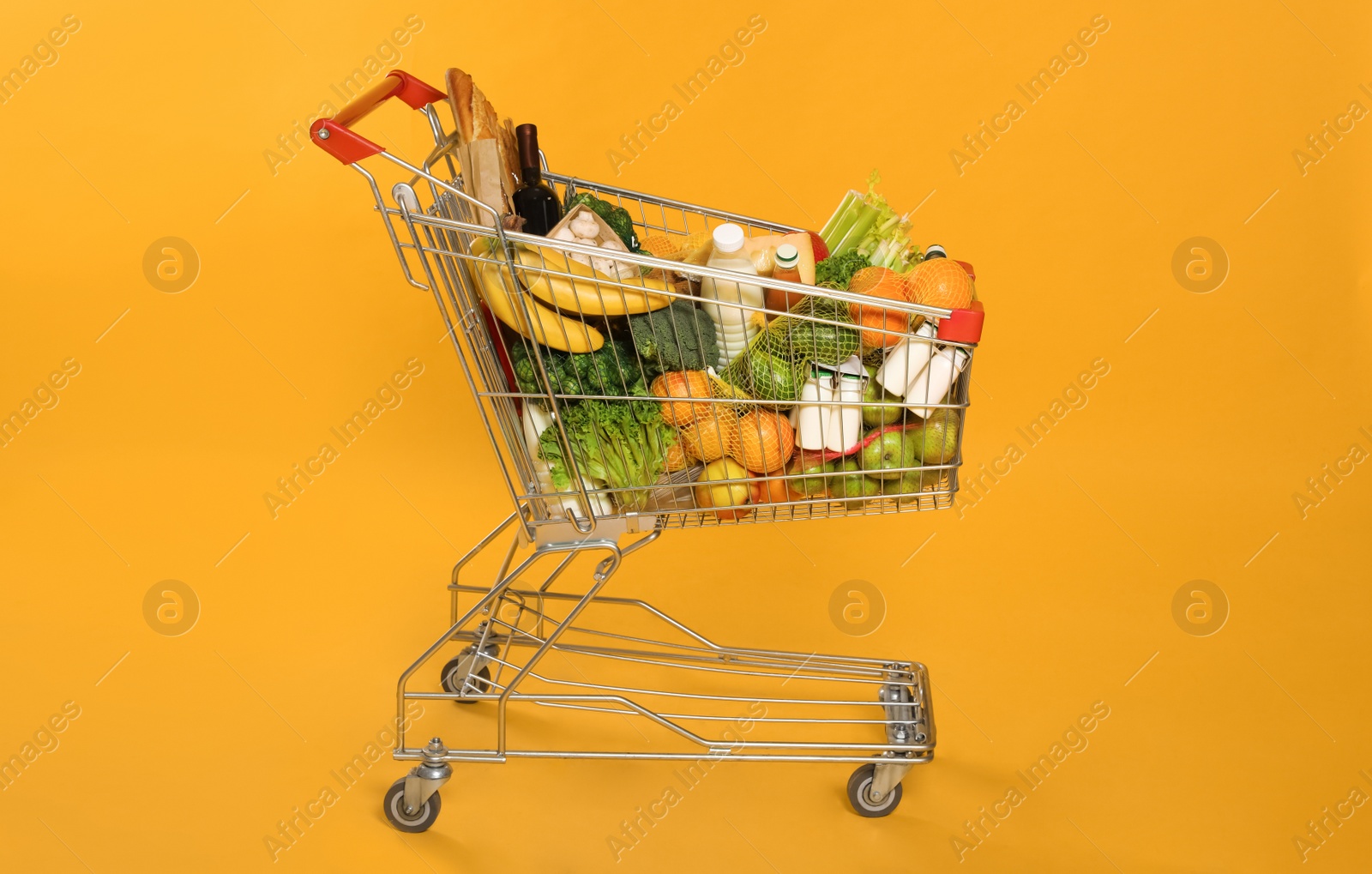 Photo of Shopping cart full of groceries on yellow background