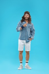 Stylish hippie man on light blue pointing at something background