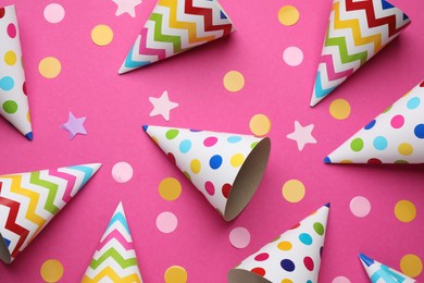 Photo of Bright party hats and confetti on pink background, flat lay