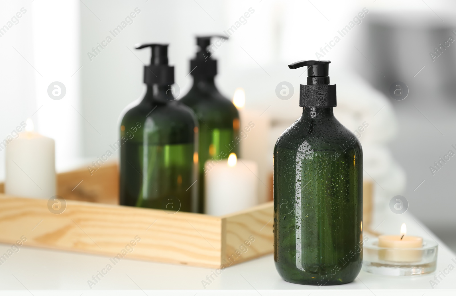 Photo of Wooden tray with soap dispensers and burning candles on white table