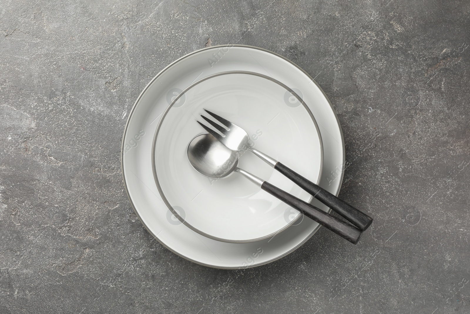 Photo of Stylish setting with cutlery and plates on grey textured table, top view