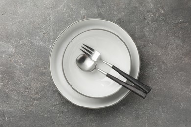 Stylish setting with cutlery and plates on grey textured table, top view