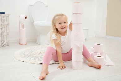 Cute little girl playing with toilet paper in bathroom