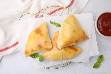 Delicious samosas with basil and tomato sauce on white table, flat lay