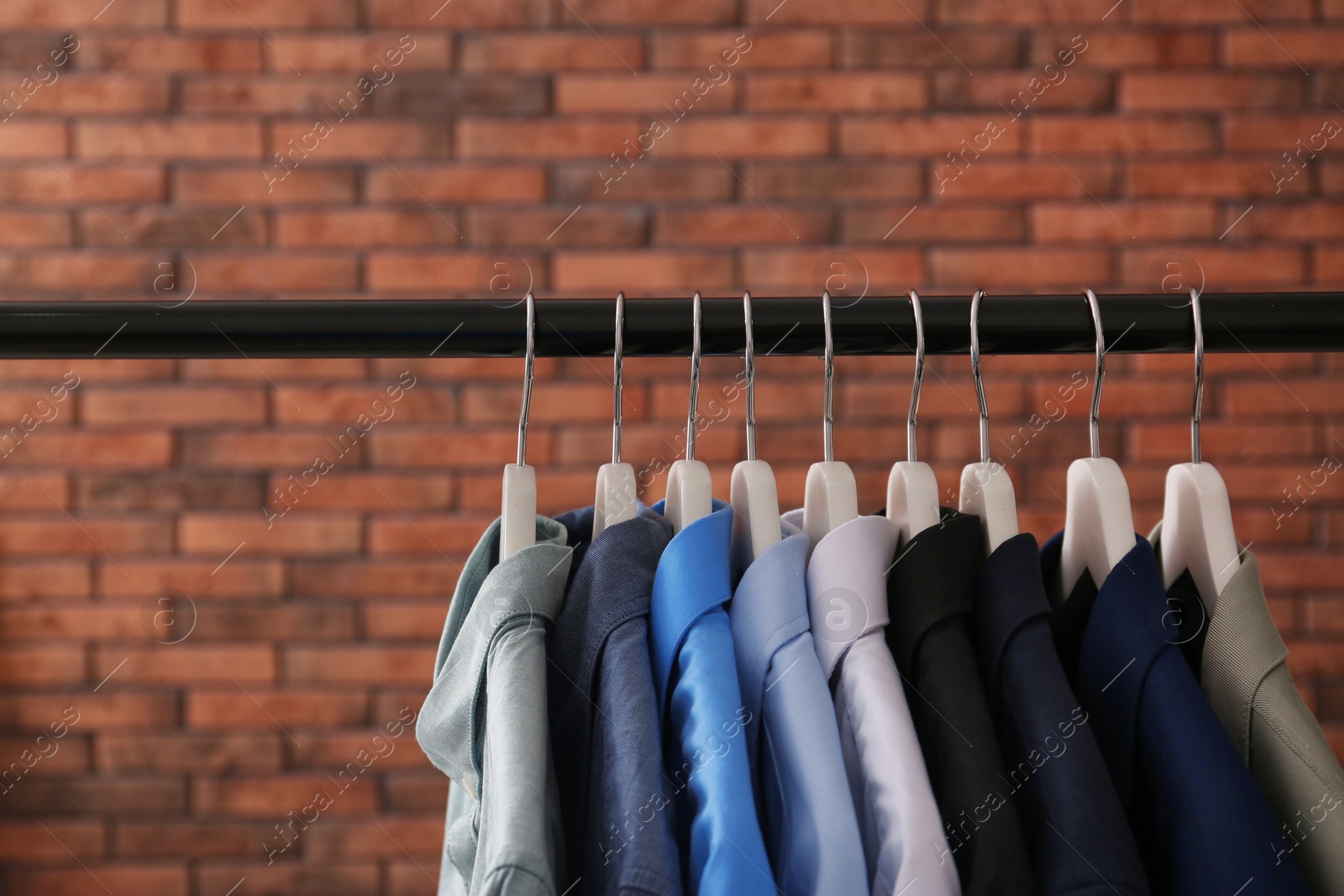 Photo of Wardrobe rack with stylish clothes near brick wall. Space for text