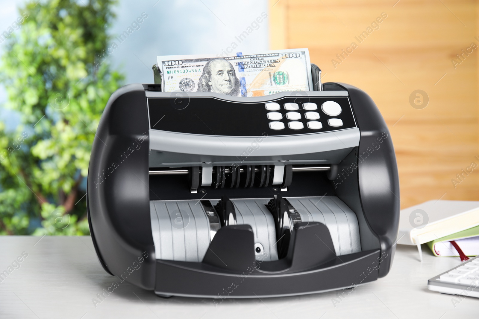 Photo of Modern electronic bill counter with money on table indoors