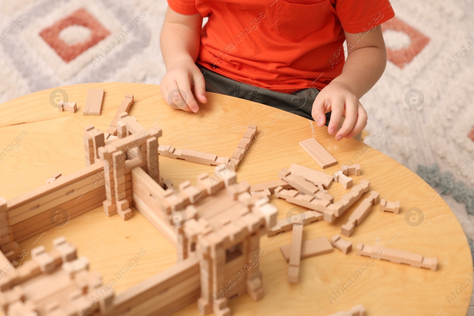 Photo of Little boy playing with wooden construction set at table in room, closeup. Child's toy