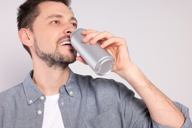 Photo of Happy man drinking from tin can on light grey background