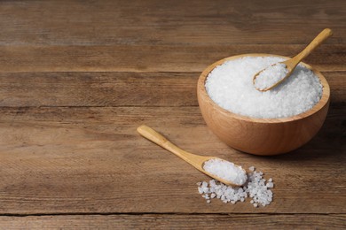 Photo of Spoons and bowl of natural sea salt on wooden table. Space for text