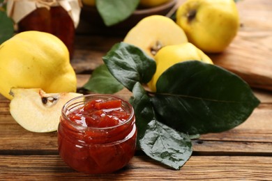 Delicious quince jam and fruits with leaves on wooden table, closeup