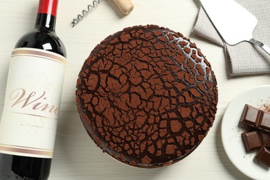Photo of Delicious truffle cake, chocolate pieces, red wine and server on light wooden table, top view