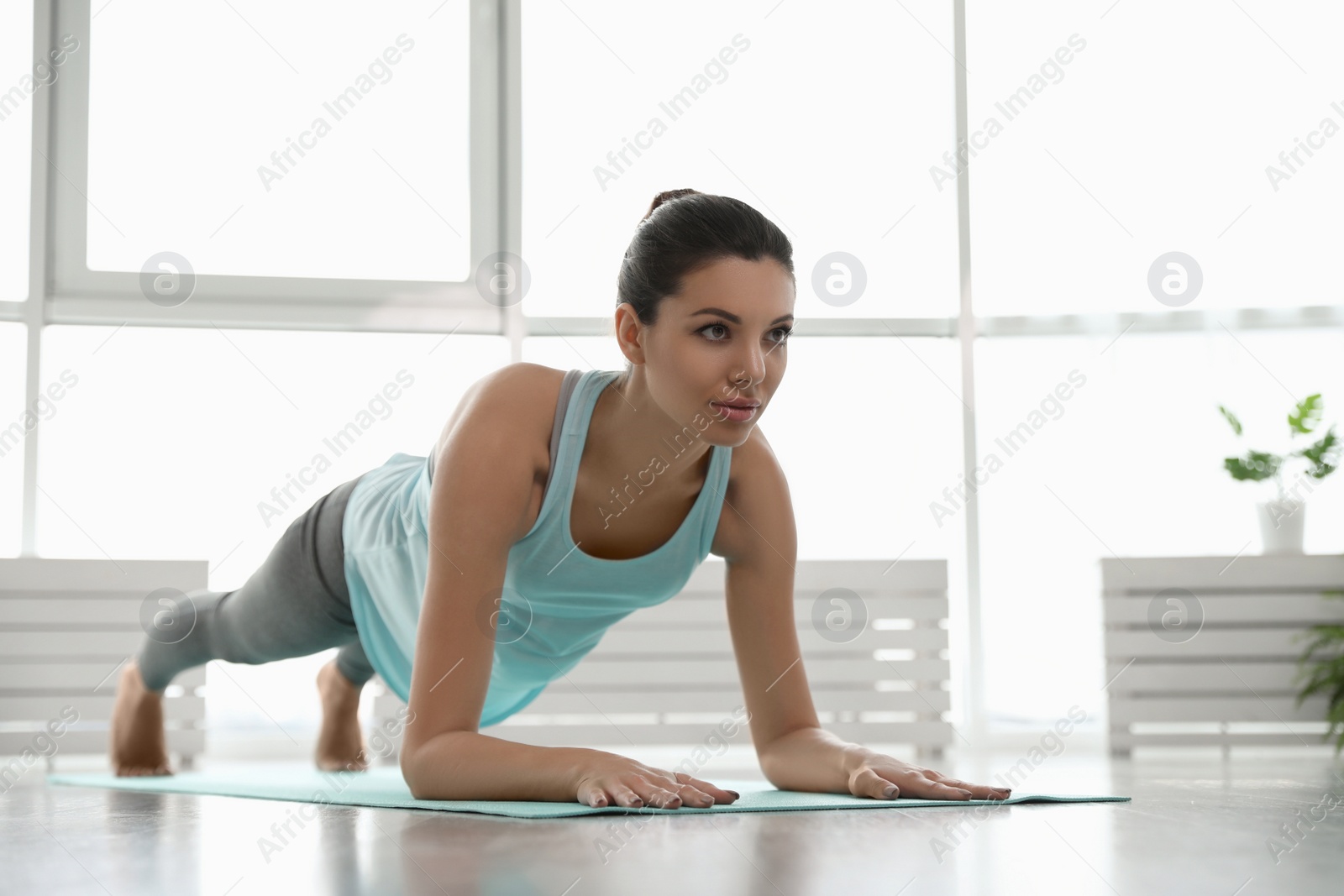 Photo of Young woman practicing forearm plank asana in yoga studio. Phalakasana variation pose