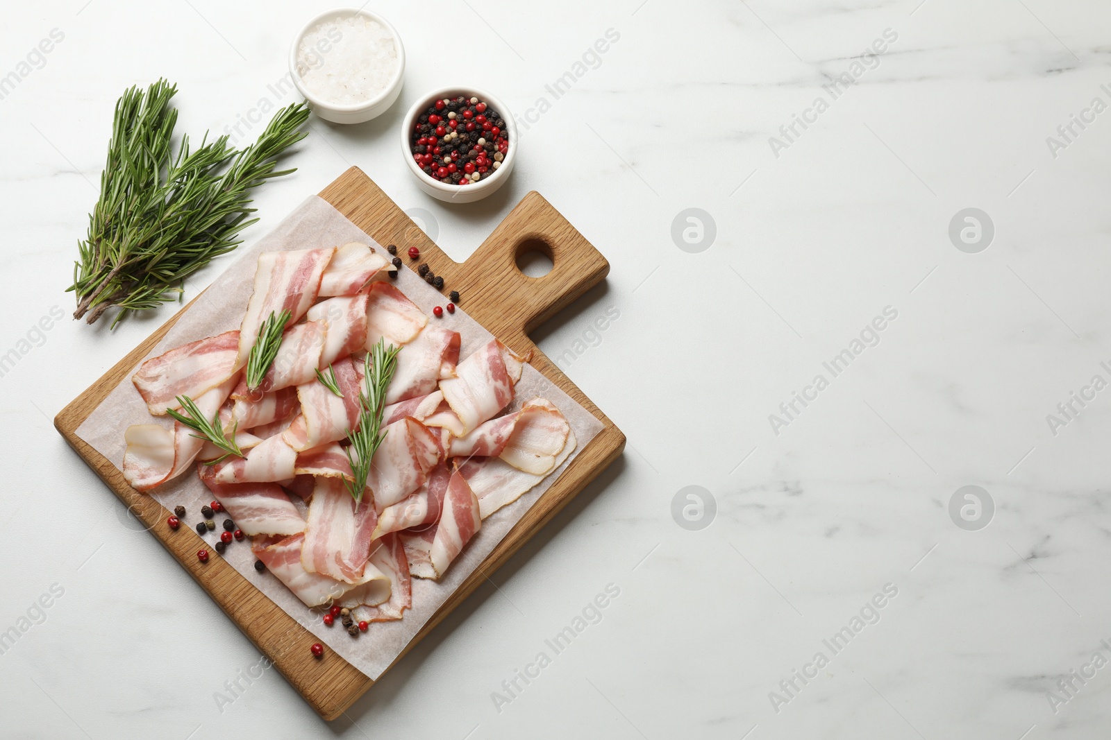 Photo of Slices of raw bacon and spices on white marble table, flat lay. Space for text