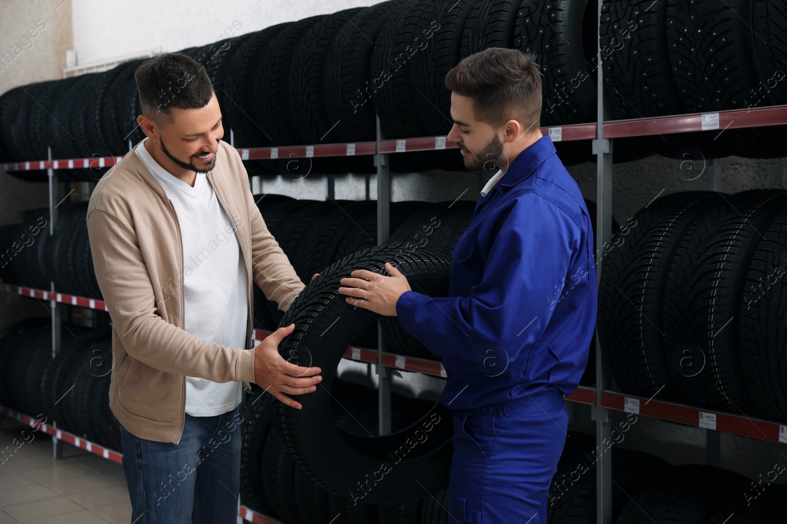 Photo of Mechanic helping client to choose car tire in auto store