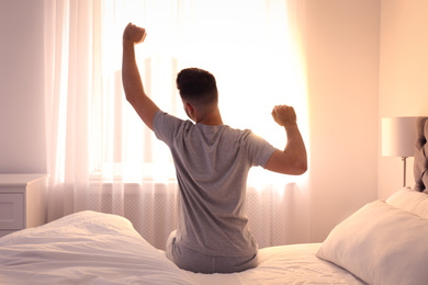 Photo of Young man stretching on bed at home, view from back. Lazy morning