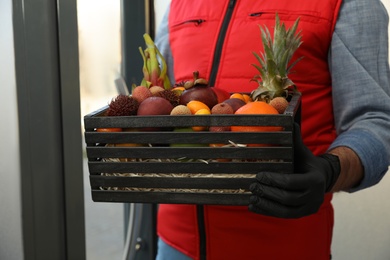 Courier holding crate with assortment of exotic fruits outdoors, closeup