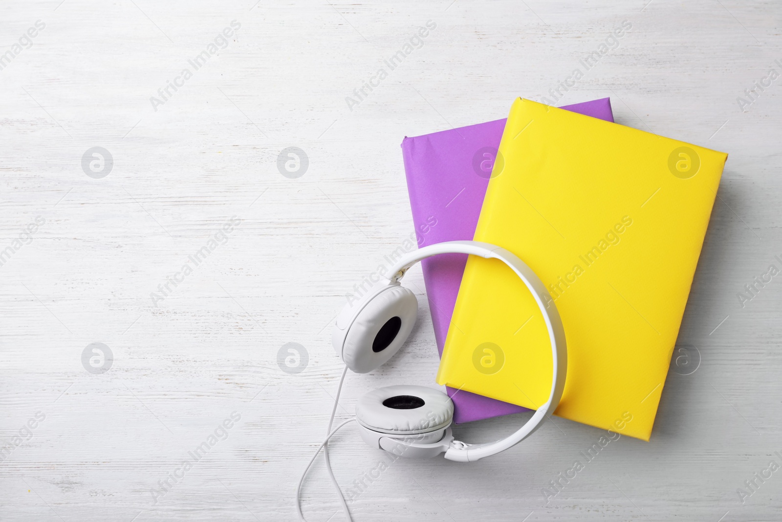 Photo of Modern headphones with hardcover books on wooden background, top view. Space for text