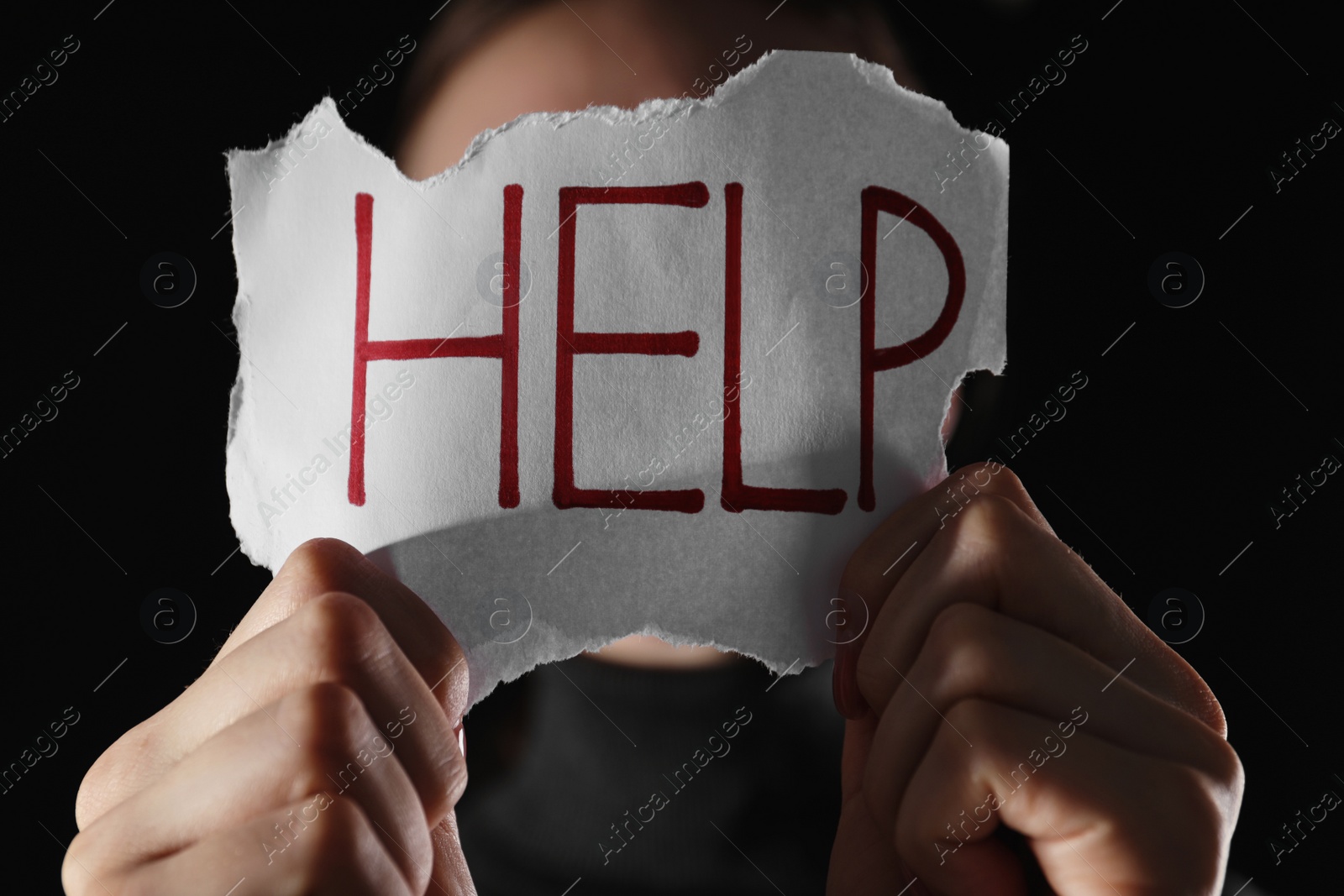 Photo of Woman holding piece of paper with word Help on black background, closeup. Domestic violence concept