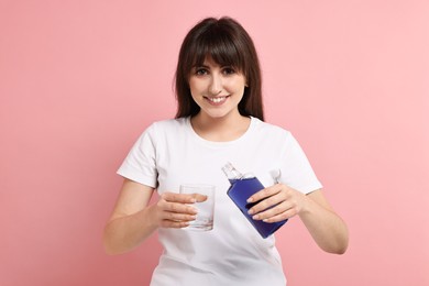 Young woman with mouthwash on pink background