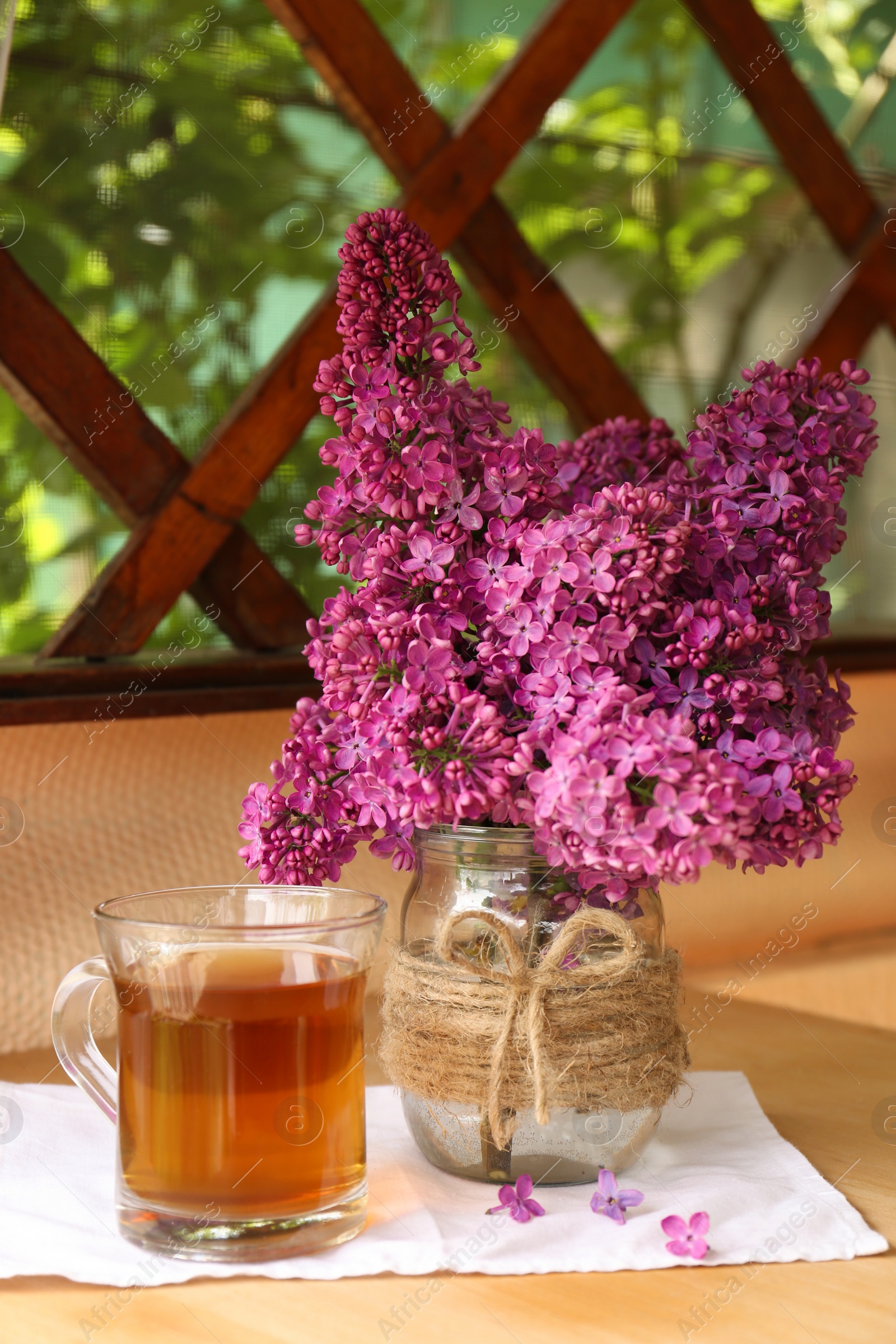 Photo of Bouquet with beautiful lilac flowers and glass cup of tea on wooden table indoors