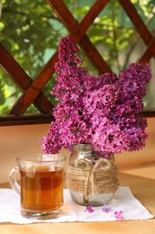 Photo of Bouquet with beautiful lilac flowers and glass cuptea on wooden table indoors