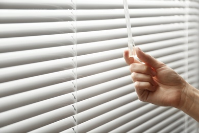 Woman opening window blinds, closeup. Space for text