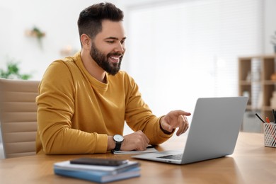 Photo of Young man using video chat during webinar at table in room